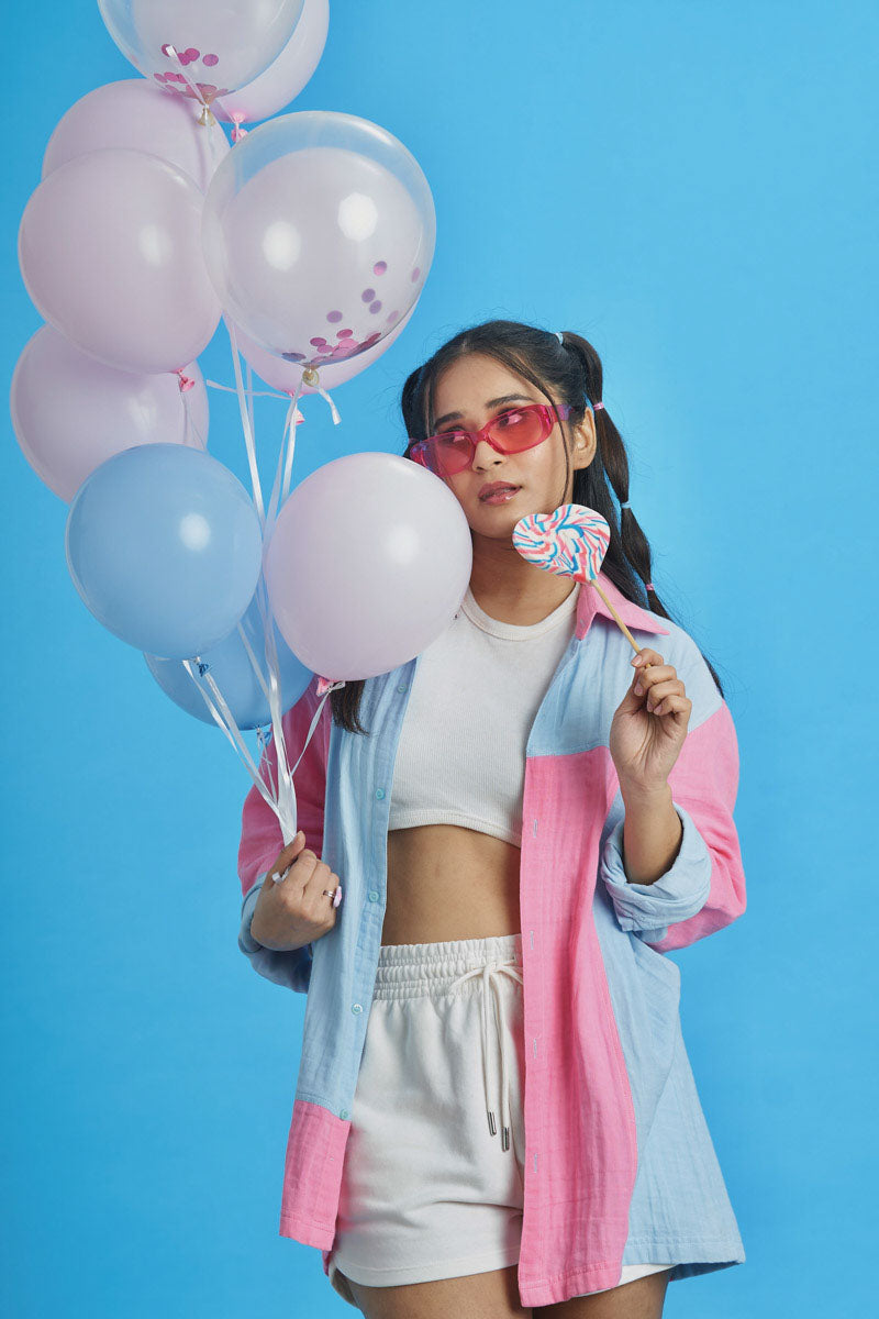 Girl wearing a loungewear patchwork shirt with pink and blue fabric patches as a jacket with red glasses with balloons behind her